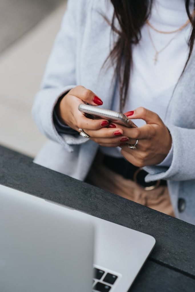 Crop ethnic businesswoman surfing internet on smartphone near laptop outdoors